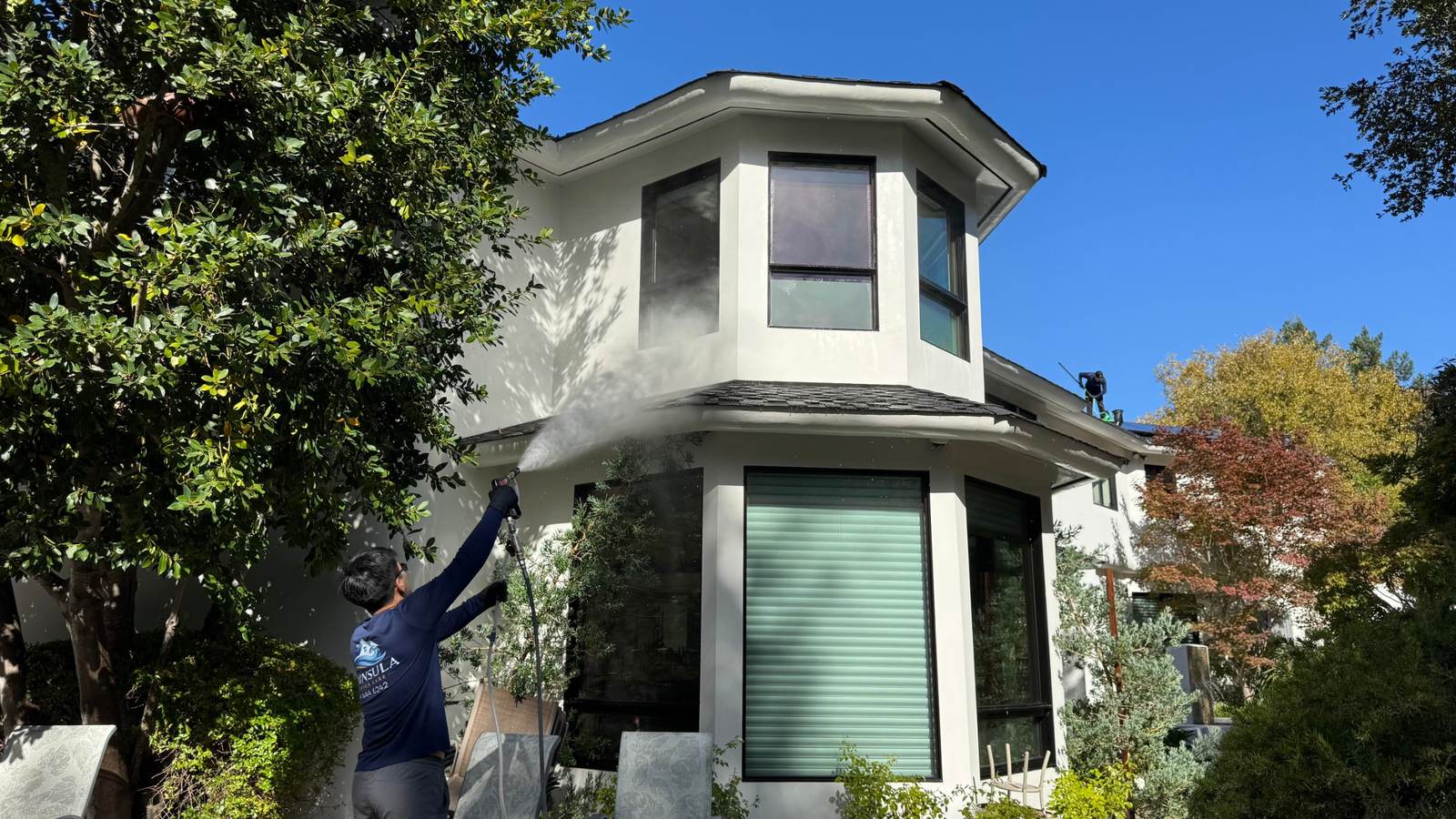 Peninsula Exterior Care technician soft washing the second story of a white stucco home